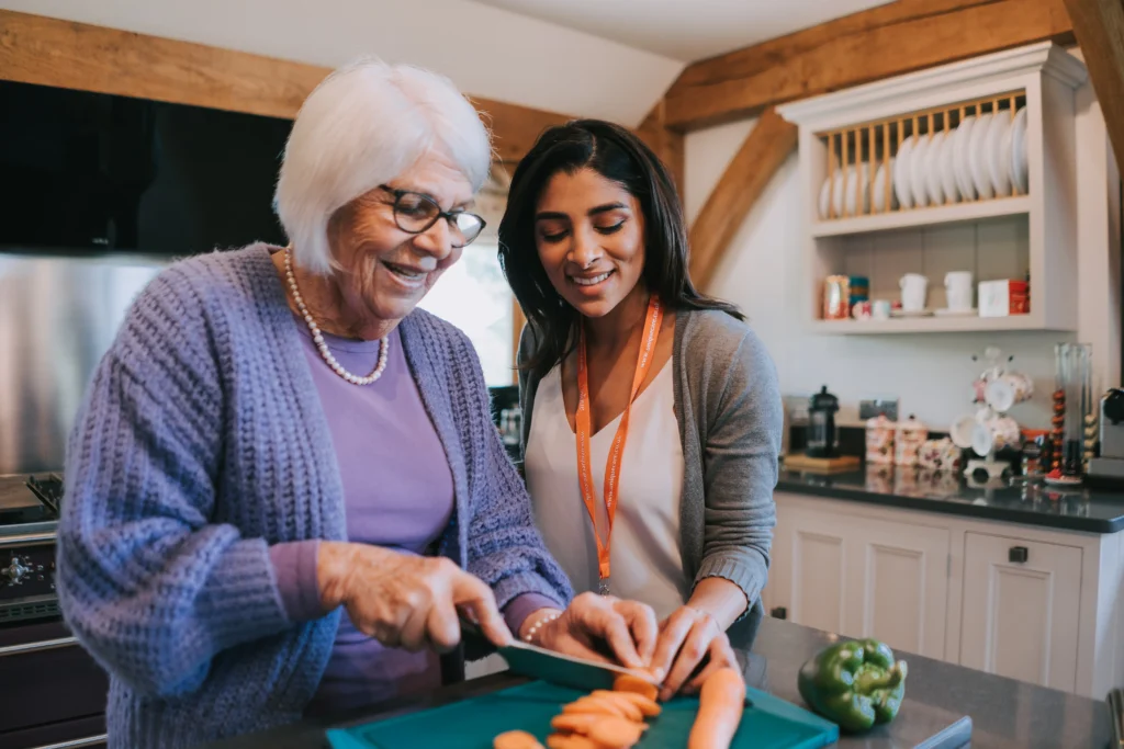 A carer and client smiling while cooking together