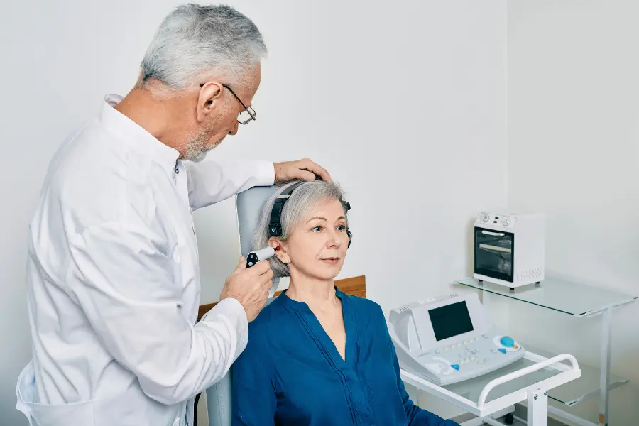 A female patient having a hearing test, wearing headphones while a healthcare professional adjusts the equipment.